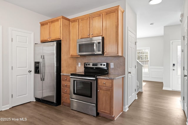 kitchen featuring appliances with stainless steel finishes, tasteful backsplash, stone countertops, and wood finished floors