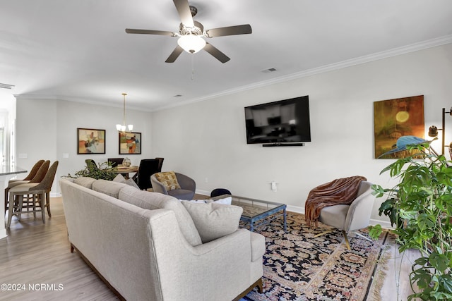 living room with ceiling fan with notable chandelier, ornamental molding, and light hardwood / wood-style floors