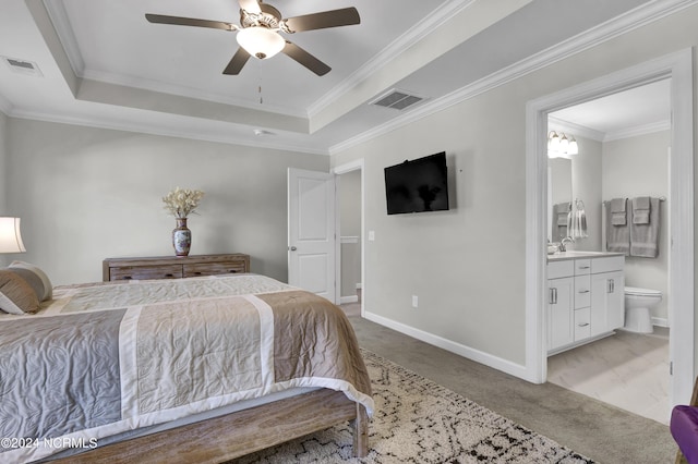 bedroom with ornamental molding, a tray ceiling, ensuite bathroom, and light carpet