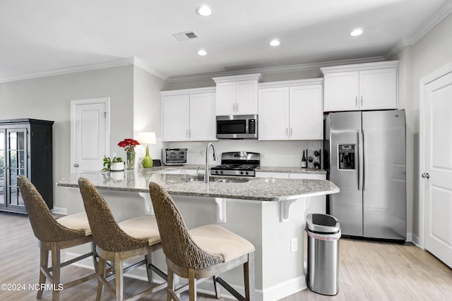 kitchen featuring a breakfast bar area, white cabinetry, crown molding, stainless steel appliances, and light stone countertops