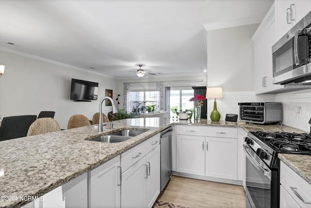 kitchen with sink, light stone counters, appliances with stainless steel finishes, kitchen peninsula, and white cabinets