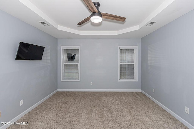 carpeted empty room with a raised ceiling and ceiling fan