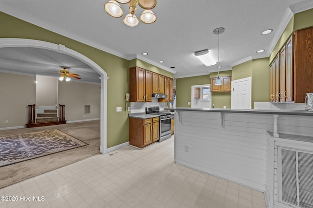 kitchen with stainless steel gas stove, arched walkways, brown cabinets, and ornamental molding