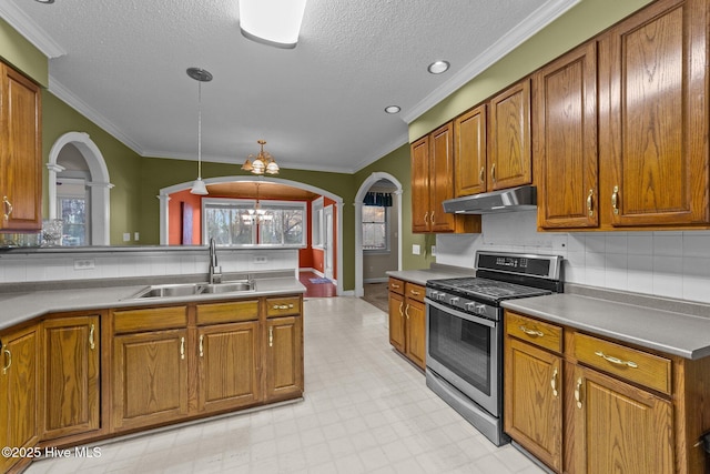 kitchen featuring stainless steel gas stove, a sink, under cabinet range hood, brown cabinetry, and light floors