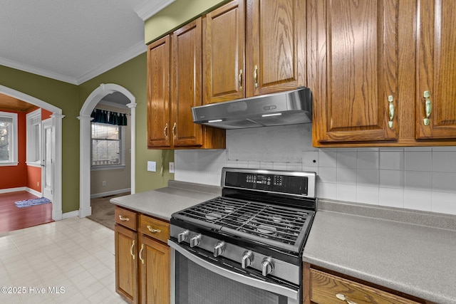 kitchen featuring under cabinet range hood, stainless steel range with gas stovetop, ornamental molding, brown cabinets, and arched walkways