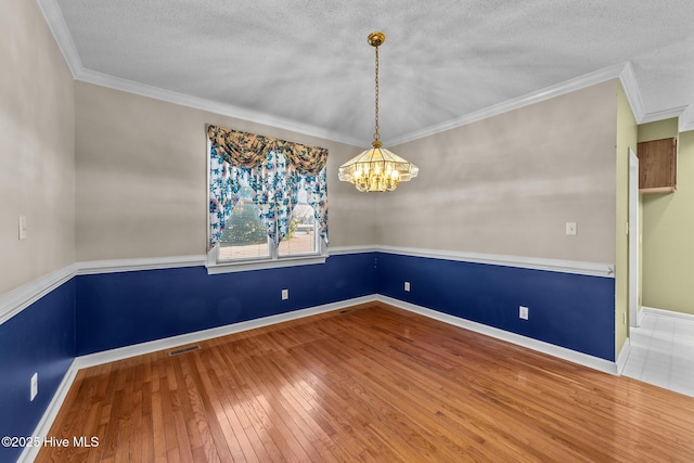 unfurnished room featuring a notable chandelier, visible vents, ornamental molding, and hardwood / wood-style floors