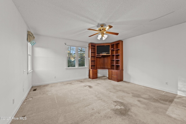 carpeted empty room with baseboards, a textured ceiling, ceiling fan, and built in study area