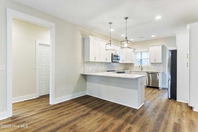 kitchen with decorative light fixtures, kitchen peninsula, stainless steel appliances, decorative backsplash, and white cabinets