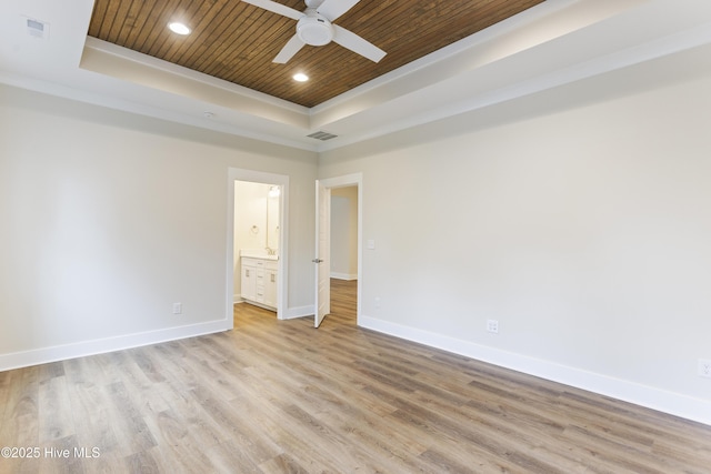 empty room with connected bathroom, wood ceiling, a tray ceiling, and light wood-type flooring