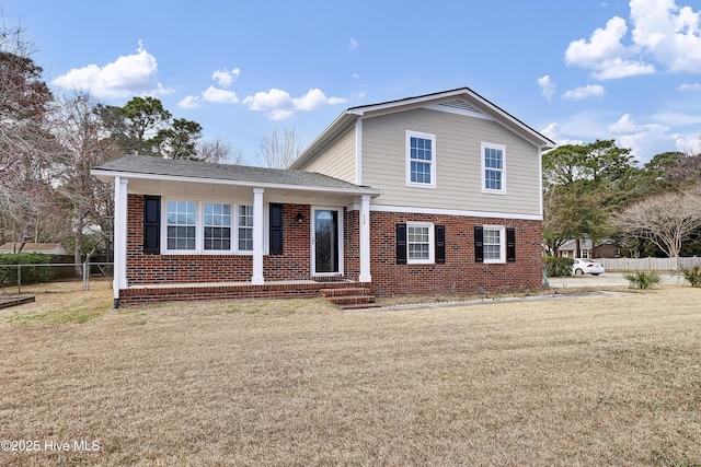 tri-level home featuring brick siding, a front lawn, and fence