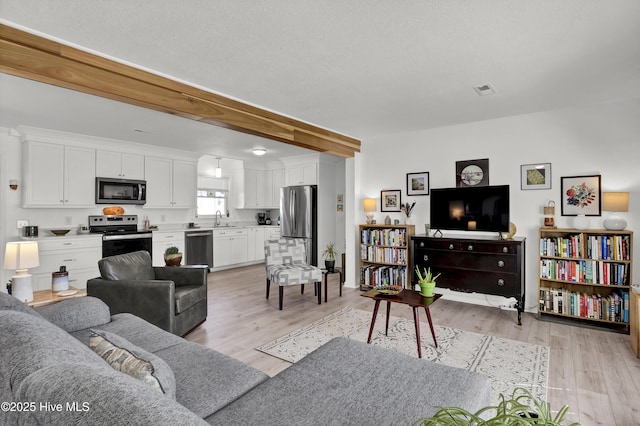 living room featuring light wood-style floors, visible vents, and beamed ceiling