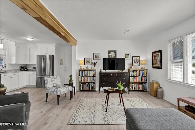 living room featuring beam ceiling, visible vents, light wood-style flooring, and a textured ceiling