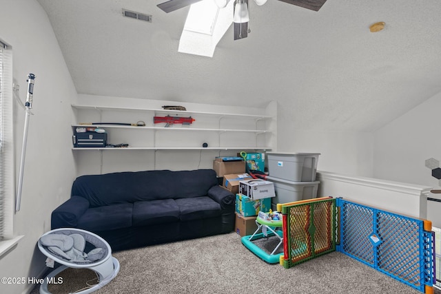 recreation room featuring ceiling fan, a textured ceiling, carpet floors, and vaulted ceiling with skylight