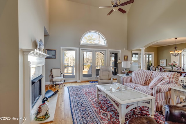 living room featuring decorative columns, a high ceiling, hardwood / wood-style floors, crown molding, and ceiling fan with notable chandelier