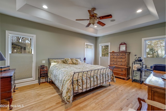 bedroom featuring multiple windows, light hardwood / wood-style flooring, and a tray ceiling