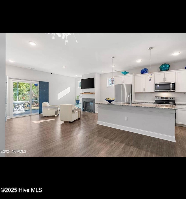 kitchen featuring white cabinetry, decorative light fixtures, a center island with sink, stainless steel appliances, and light stone countertops