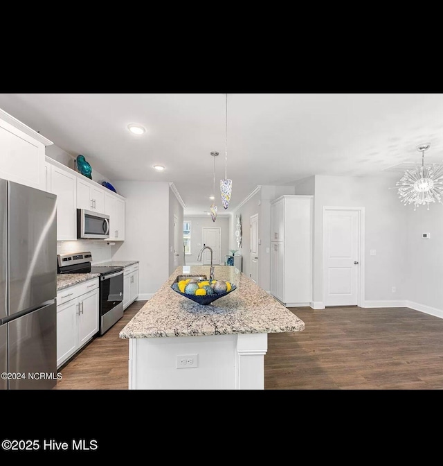 kitchen featuring white cabinetry, light stone counters, a center island with sink, pendant lighting, and stainless steel appliances