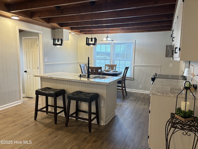 kitchen with dark hardwood / wood-style floors, decorative light fixtures, a center island with sink, and white cabinets