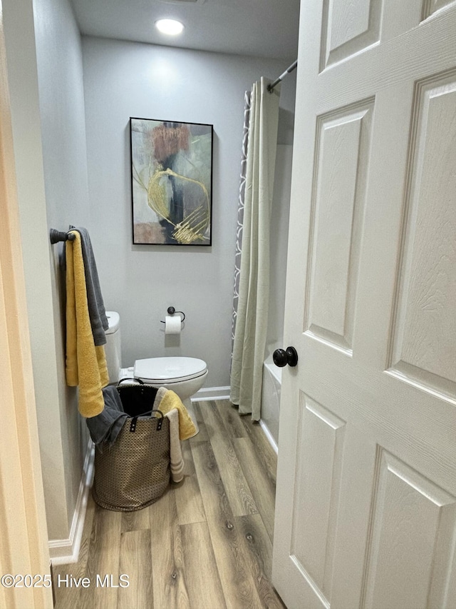 bathroom with hardwood / wood-style floors, toilet, and shower / bath combo with shower curtain