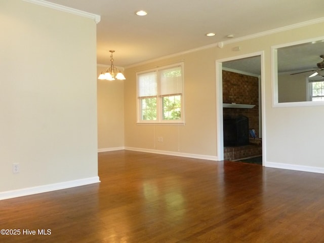 unfurnished room with ceiling fan with notable chandelier, ornamental molding, dark hardwood / wood-style floors, and a fireplace