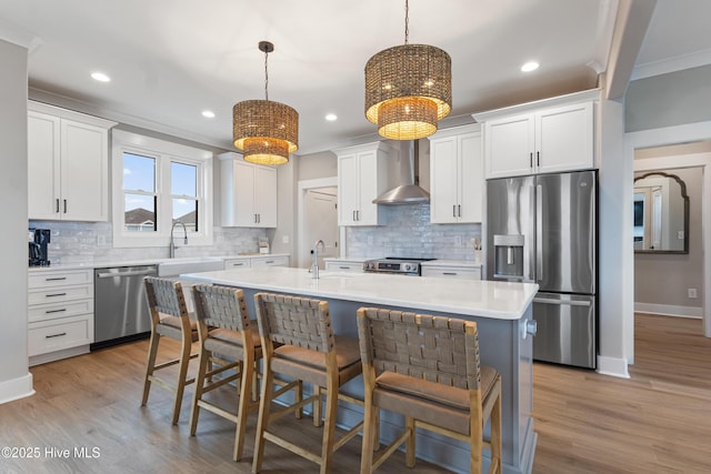 kitchen featuring wall chimney range hood, appliances with stainless steel finishes, hanging light fixtures, a center island, and white cabinets