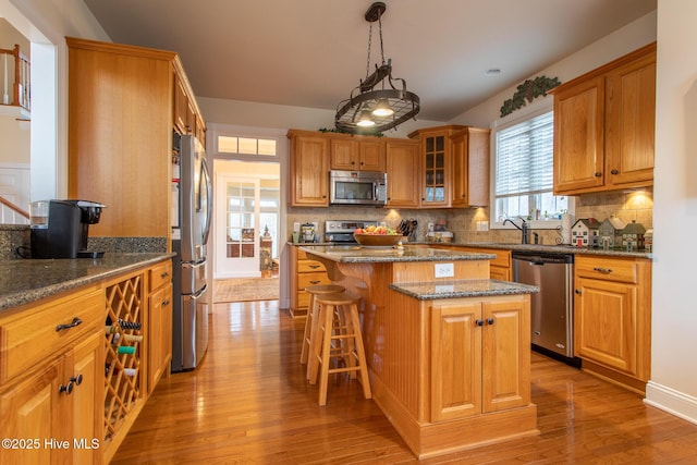 kitchen featuring appliances with stainless steel finishes, backsplash, hanging light fixtures, a center island, and light hardwood / wood-style floors