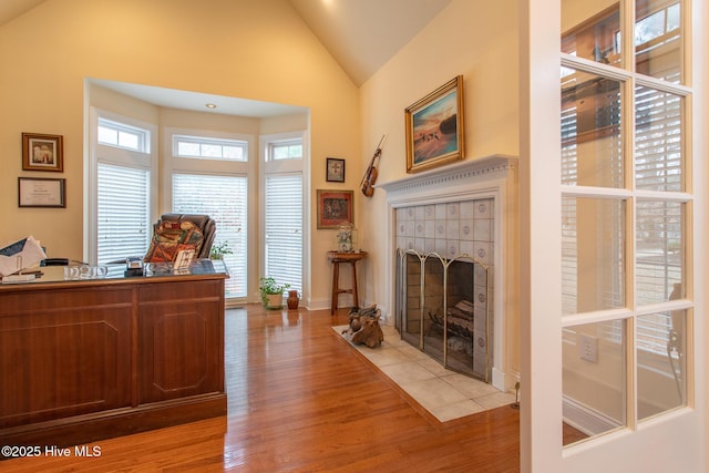 office featuring a tiled fireplace, light hardwood / wood-style flooring, and high vaulted ceiling