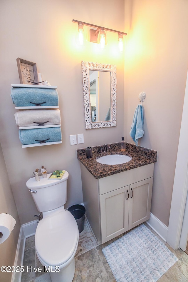 half bathroom with baseboards, vanity, and toilet