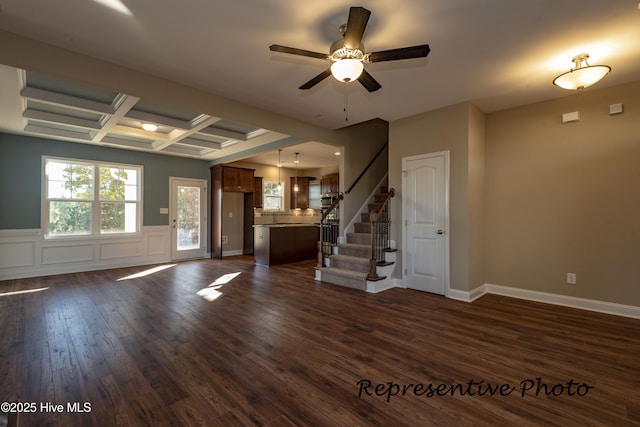 unfurnished living room featuring stairway, a ceiling fan, dark wood-style flooring, coffered ceiling, and beamed ceiling