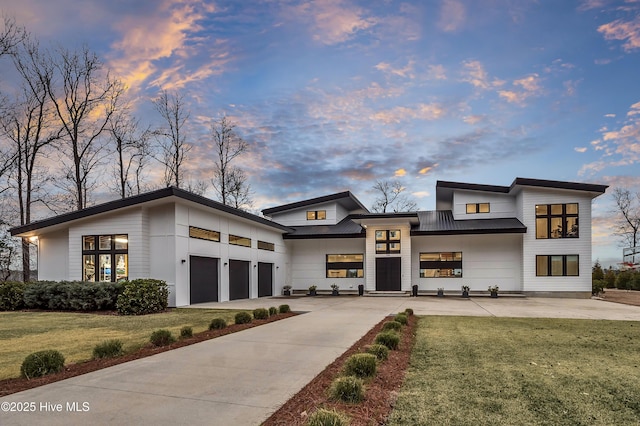 contemporary home featuring metal roof, an attached garage, concrete driveway, a lawn, and a standing seam roof