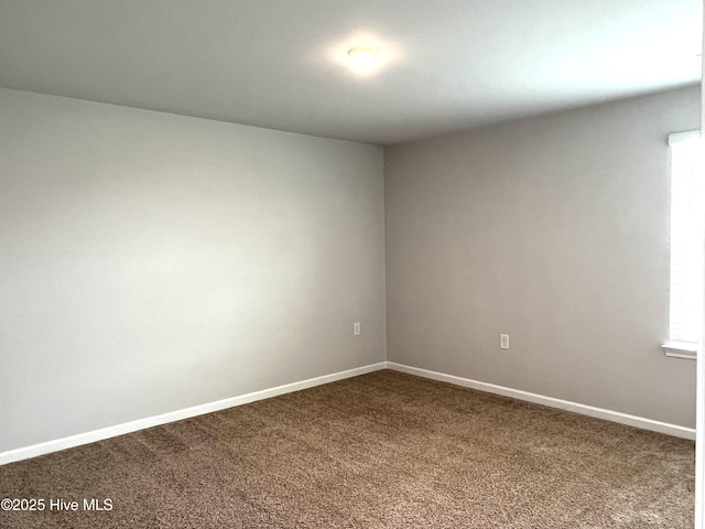 spare room featuring dark carpet and baseboards