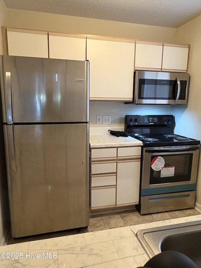 kitchen with white cabinetry, stainless steel appliances, and a textured ceiling