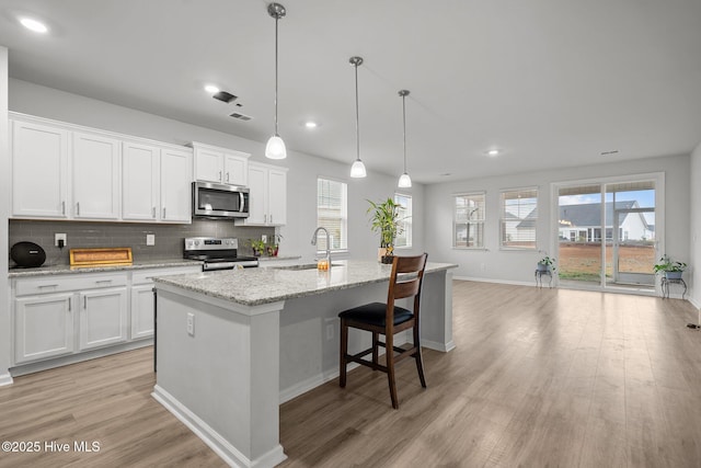 kitchen with white cabinetry, sink, stainless steel appliances, and a center island with sink