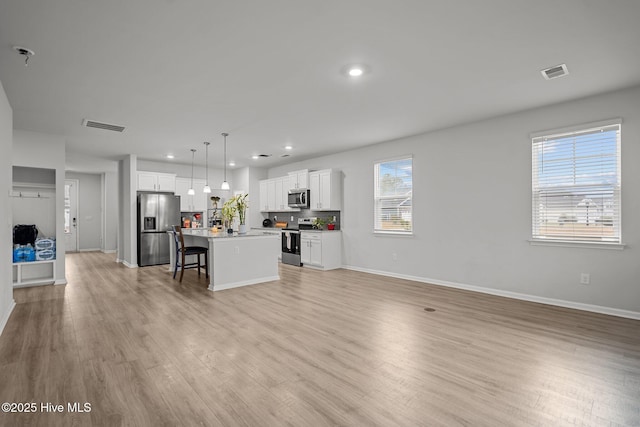 kitchen featuring appliances with stainless steel finishes, white cabinetry, hanging light fixtures, a kitchen breakfast bar, and a center island