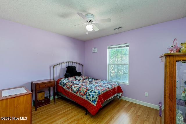 bedroom featuring baseboards, visible vents, a ceiling fan, a textured ceiling, and light wood-type flooring