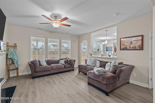 living room with ceiling fan with notable chandelier, light hardwood / wood-style floors, and a textured ceiling