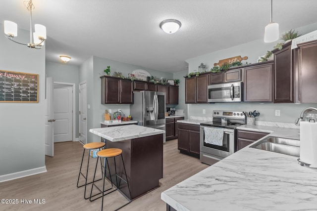 kitchen with decorative light fixtures, dark brown cabinets, light hardwood / wood-style flooring, a kitchen island, and stainless steel appliances