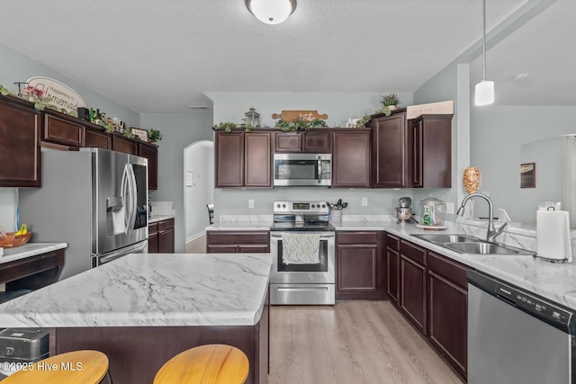 kitchen featuring sink, hanging light fixtures, light wood-type flooring, appliances with stainless steel finishes, and a kitchen breakfast bar