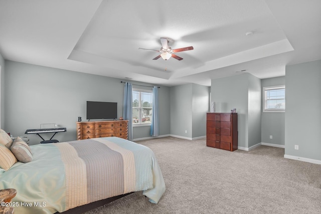 bedroom with ceiling fan, a raised ceiling, light carpet, and multiple windows