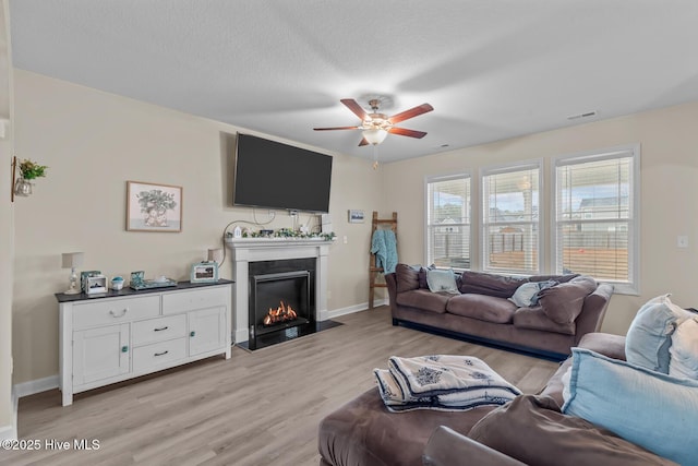 living room featuring ceiling fan, a textured ceiling, and light wood-type flooring