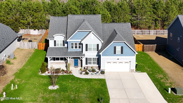 view of front facade featuring a shingled roof, concrete driveway, a front yard, fence, and stone siding