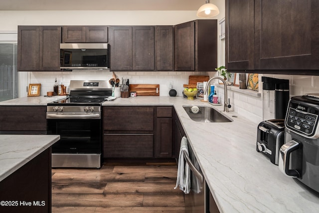 kitchen with stainless steel appliances, light stone counters, a sink, and dark brown cabinetry