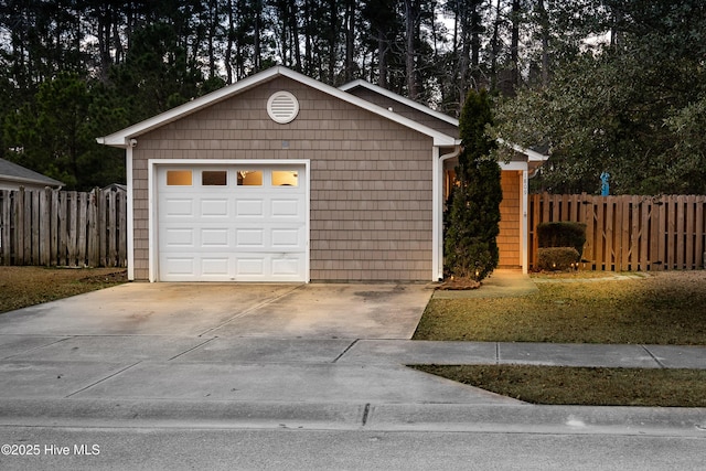 detached garage featuring concrete driveway and fence