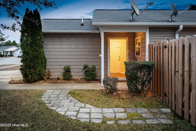 entrance to property featuring a shingled roof and fence