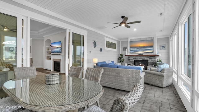 sunroom / solarium with a warm lit fireplace and ceiling fan