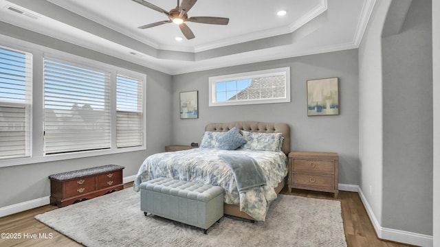 bedroom featuring a tray ceiling, baseboards, wood finished floors, and crown molding