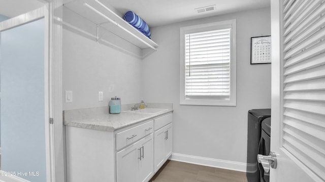 washroom featuring wood finished floors, baseboards, laundry area, a sink, and washer and clothes dryer