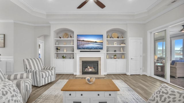 living room with light wood-type flooring, built in shelves, arched walkways, and a glass covered fireplace