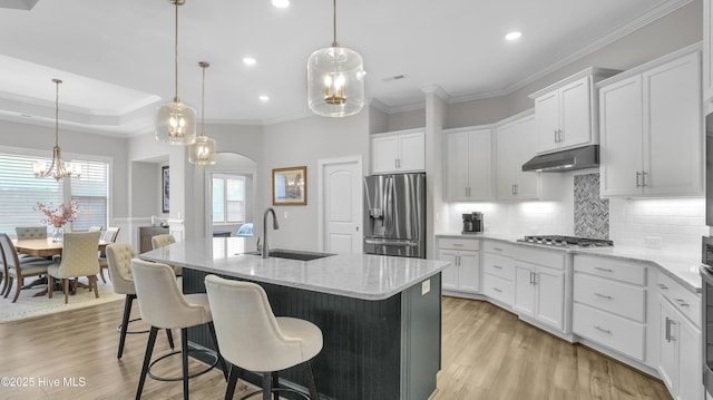 kitchen featuring arched walkways, a sink, under cabinet range hood, appliances with stainless steel finishes, and light wood-type flooring