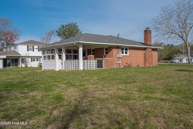 back of house featuring a shingled roof, a lawn, brick siding, and a chimney